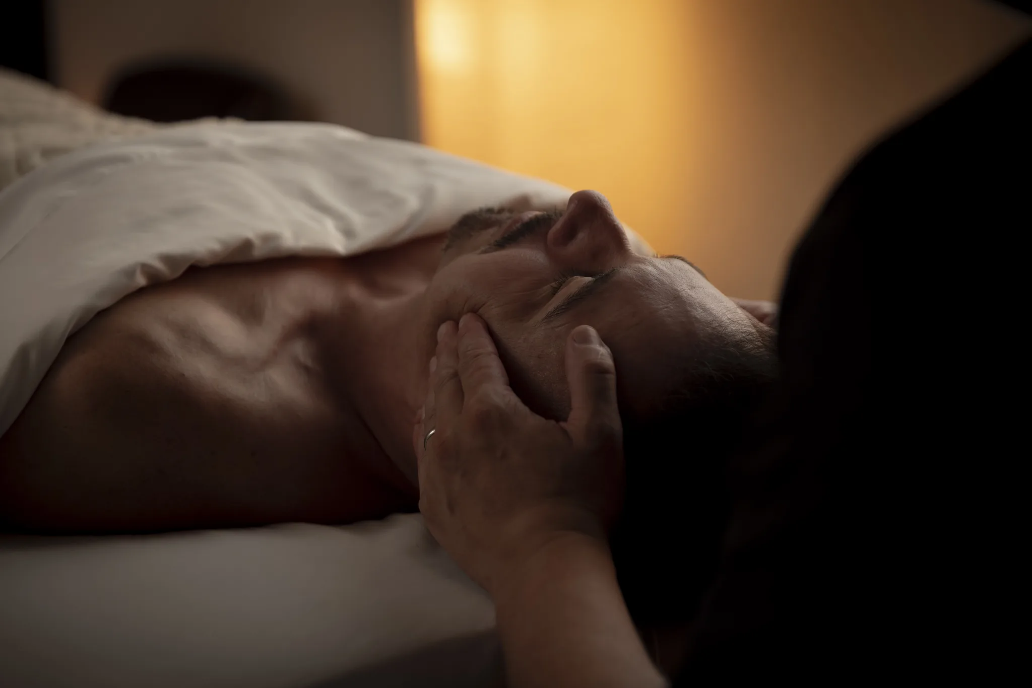 Dorian supporting a resting client's head and jaw with one hand.