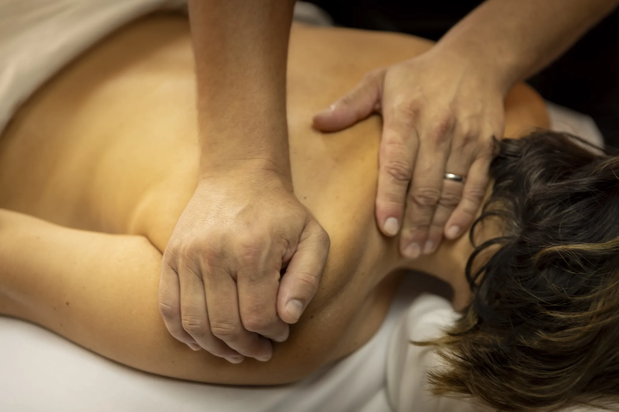 Close view of both hands working along a client's neck and shoulder.