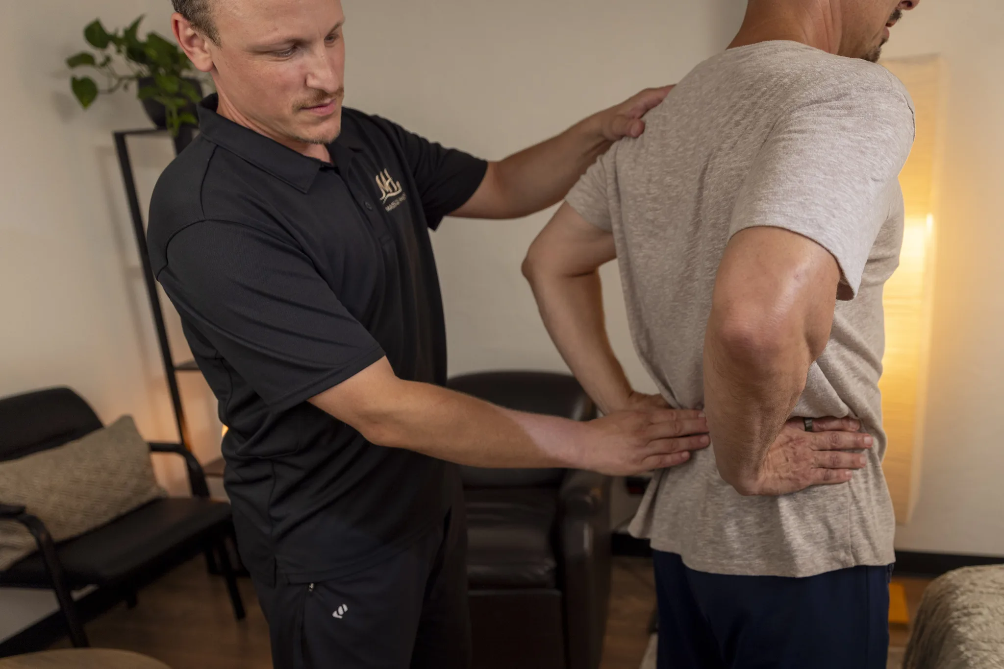 Dorian assessing a standing client's back, one hand at the shoulder and one at the lower back.