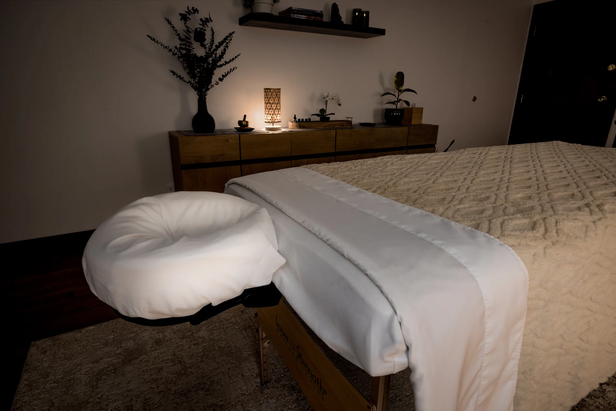 The treatment room at Massage Habits, with the table prepared and warm lamplight on the console behind.