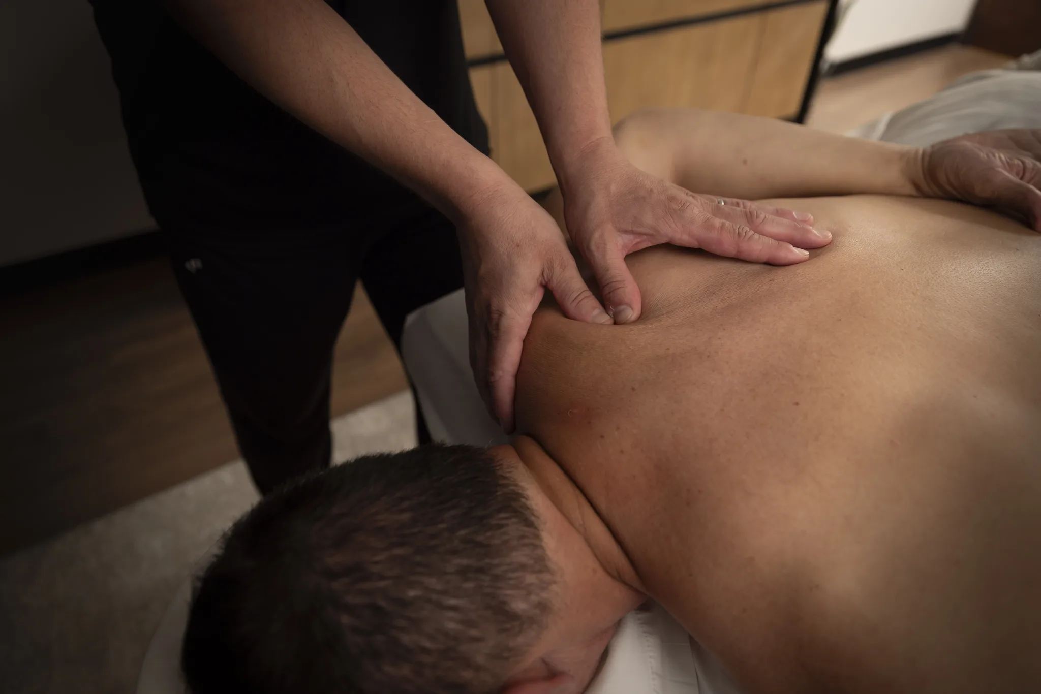 Hands working along a client's shoulder blade and upper back.